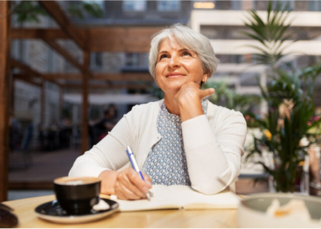 An older woman enjoying a cup of coffee and writing in a journal. 