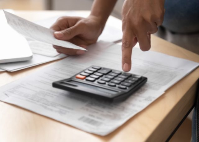 A person going through paperwork with a calculator.