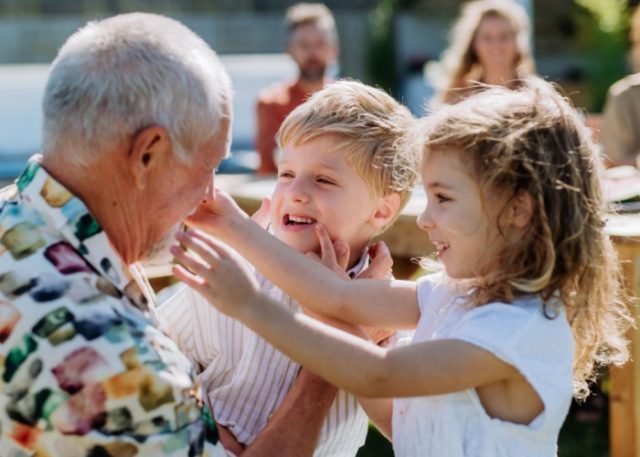 A grandfather playing with his grandchildren outdoors.