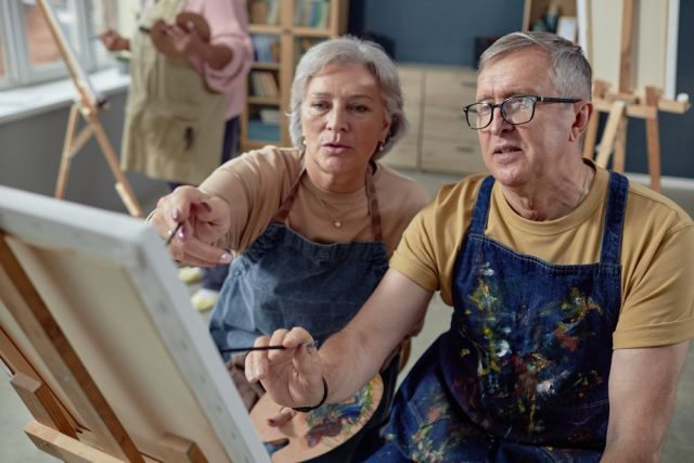 An older couple painting at an easel together.