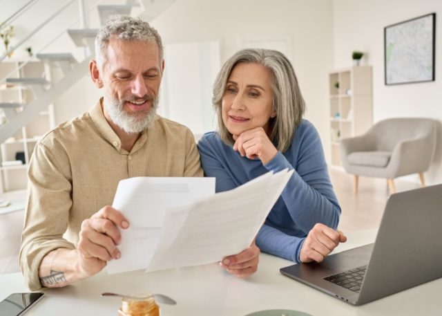 A senior couple sit at a laptop comparing multiple documents
