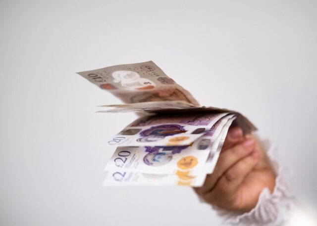 A hand holding UK bank notes.